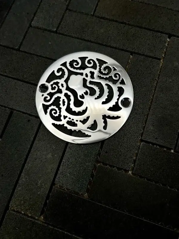 Round drain with octopus design in polished stainless steel finish.