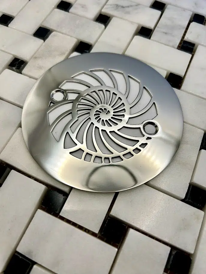 Round drain with nautilus design in polished stainless steel finish.