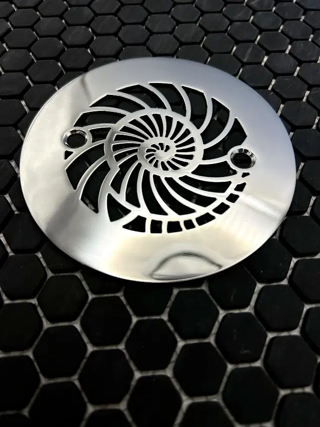 Round drain with nautilus design in polished stainless steel finish.