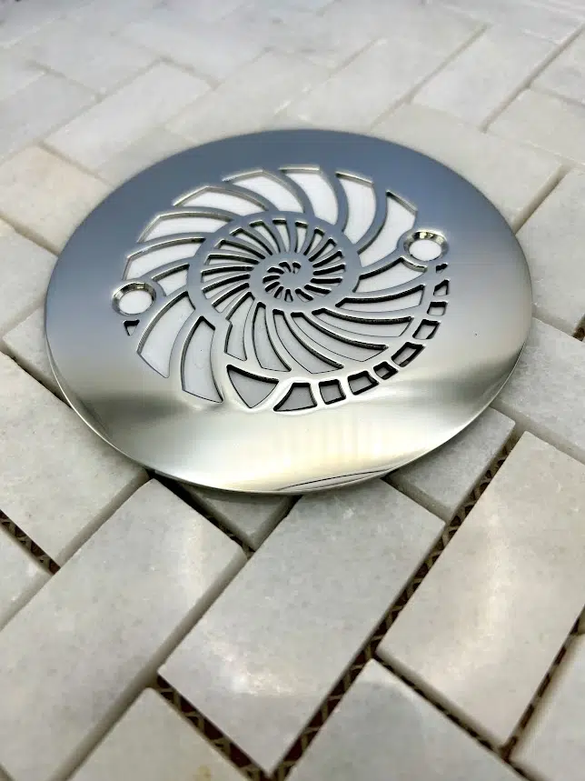 Round drain with nautilus design in polished stainless steel finish.