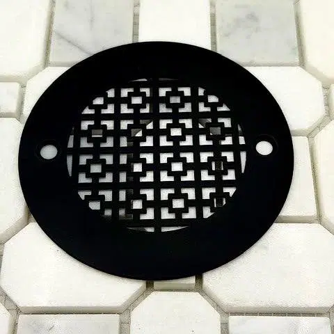 Geometric No. 1 4.25 inch round shower drain with a matte black finish on white tile.