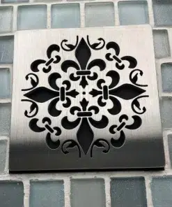 Fleur De Lis brushed stainless steel shower drain cover on blue square tile.