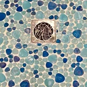 Seahorse square shower drain cover in polished stainless steel, installed on a ocean blue tile.