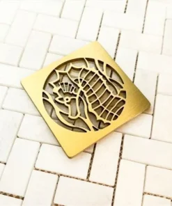 Seahorse square shower drain cover in brushed brass on white tile