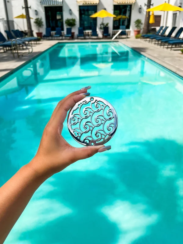 polished stainless steel NDS outdoor drain with cut out wave design, with swimming pool in the background