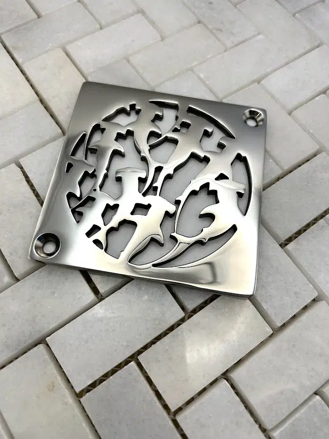 Square drain with sharks design in polished stainless steel finish.