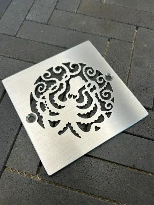 Square drain with octopus design and a brushed stainless steel finish.