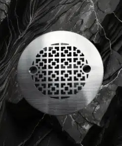 Geometric No. 1, 4.25 inch round shower drain in brushed stainless steel on black marble background.