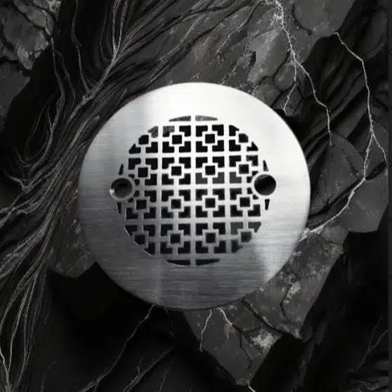 Geometric No. 1, 4.25 inch round shower drain in brushed stainless steel on black marble background.