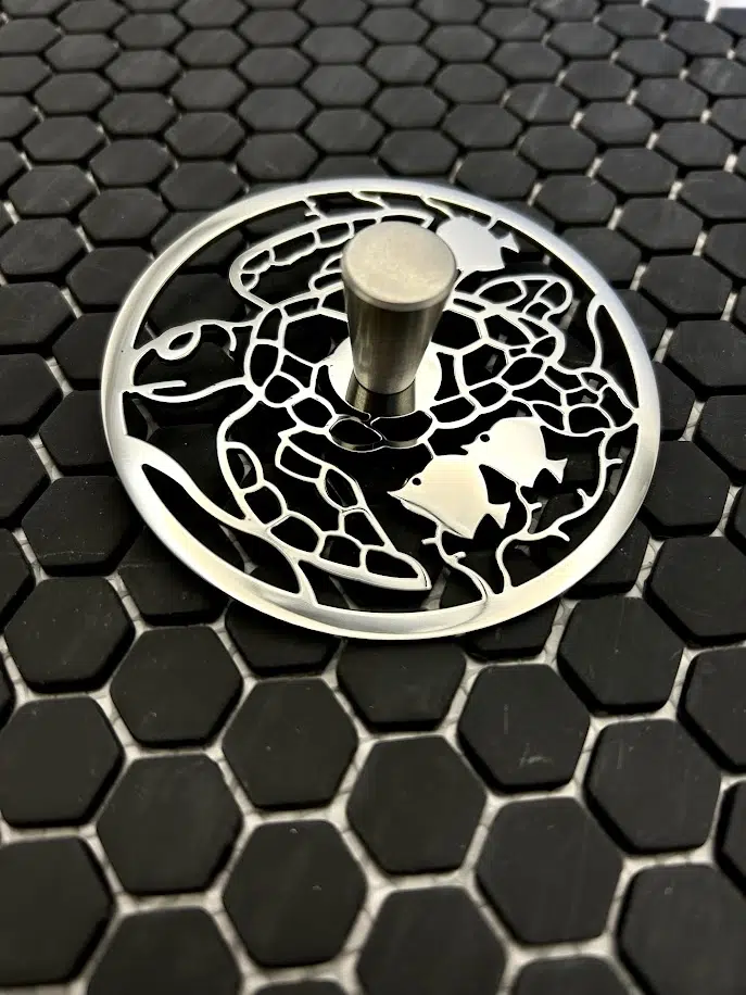 Round sink strain with turtle design in polished stainless steel finish.