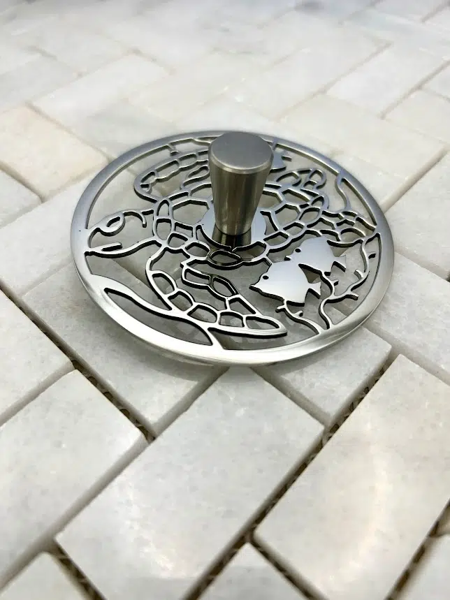 Round sink strain with turtle design in polished stainless steel finish.