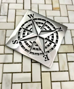 Square drain with compass rose design in polished stainless steel.