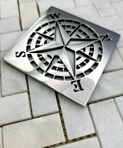Square drain with compass rose design in polished stainless steel.