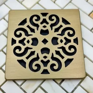 Scrolls No. 4 square shower drain in champagne bronze finish set on tile with black background